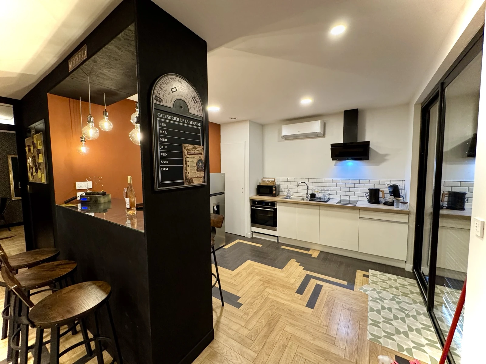 La cuisine ouverte avec four, plaques de cuisson et comptoir sous les suspensions lumineuses.
