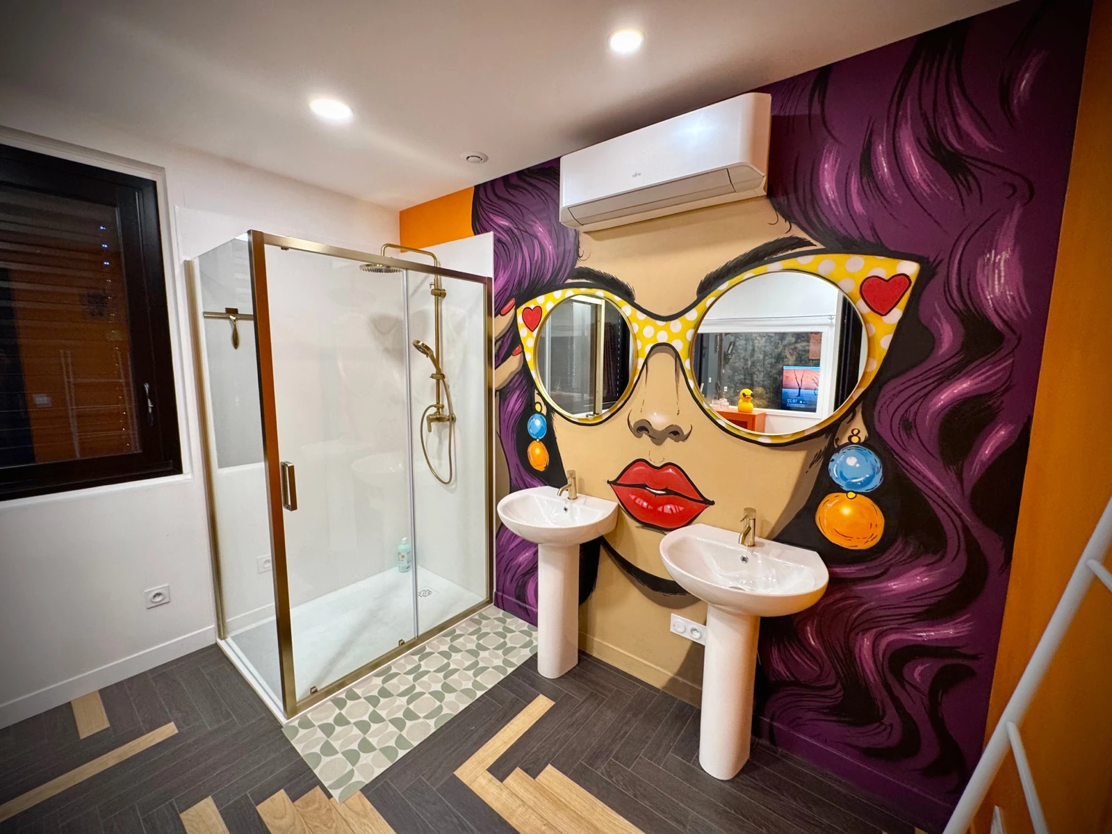 Salle de bain années 70–80 avec douche, fresque pop art et double vasque.